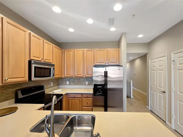 a kitchen with stainless steel appliances granite countertop a refrigerator a stove top oven a sink a dining table and chairs with wooden floor