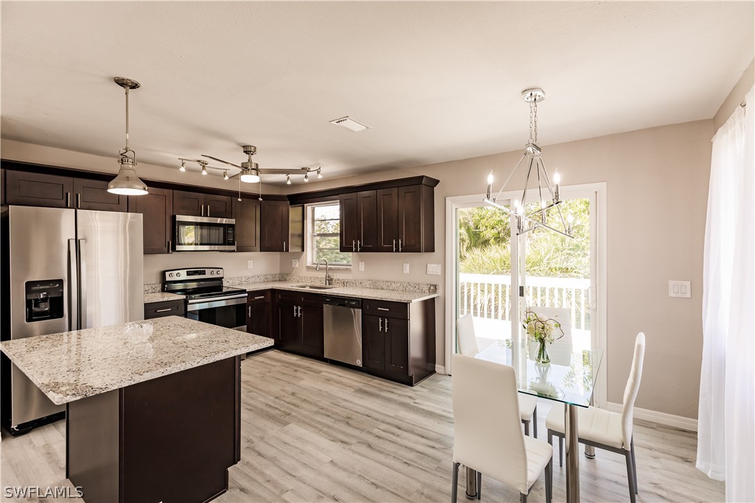 8049 Albatross Road Fort Myers, FL 33967 - Photo 22 of 35 a large kitchen with stainless steel appliances kitchen island granite countertop a table chairs and a wooden floor
