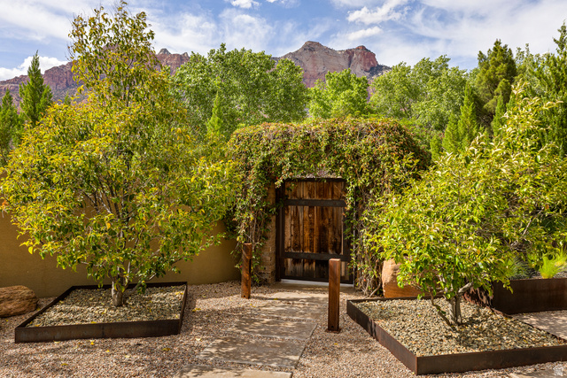 105 River Bend Circle, Unit 105 Springdale, UT 84767 - Photo 35 of 56 Enclosed courtyard featuring a rustic wooden gate, mature trees with metal-edged planters, gravel ground cover, and a stucco privacy wall