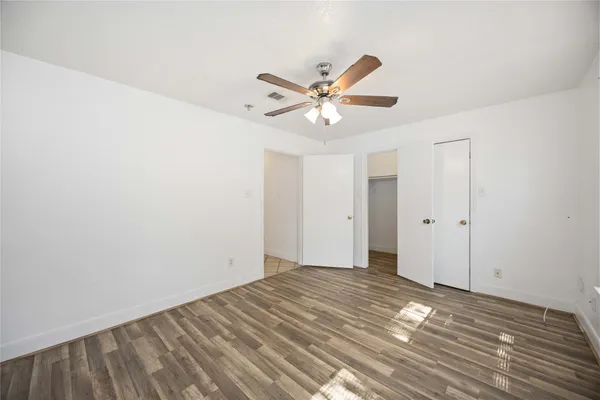an empty room with wooden floor fan and windows