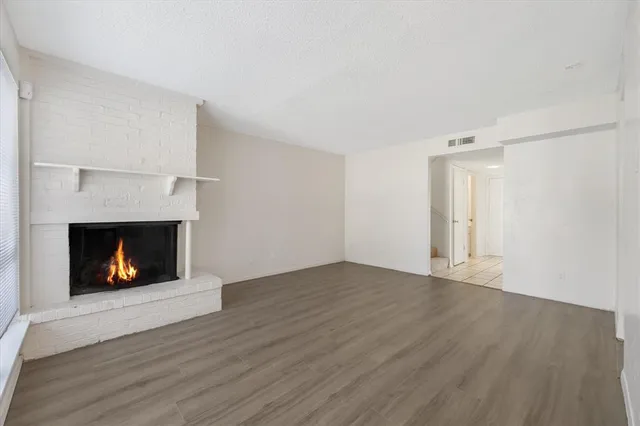 a view of an empty room with wooden floor fireplace and a window