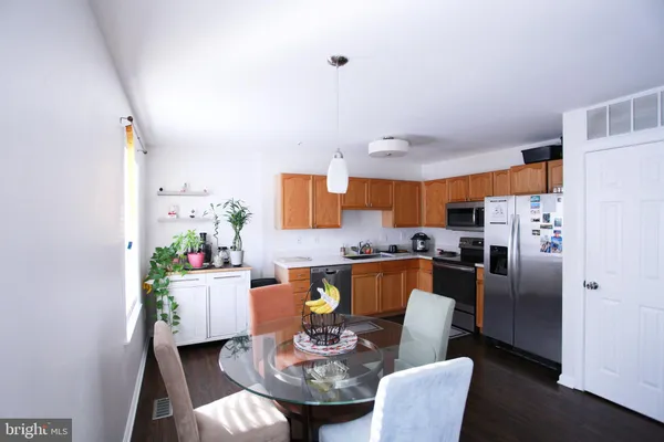 a kitchen with stainless steel appliances granite countertop a refrigerator a sink a stove a dining table and chairs with wooden floor