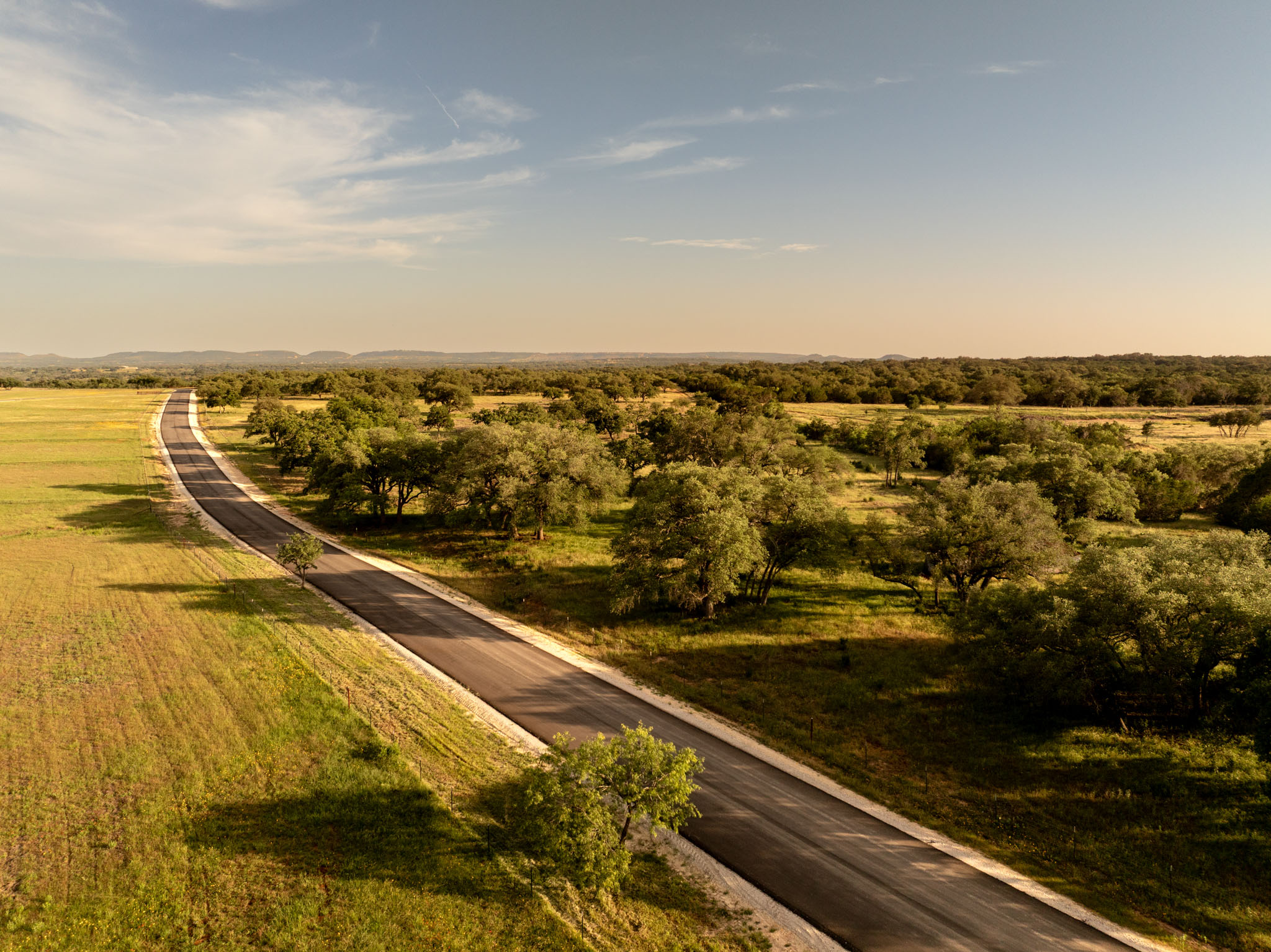 1701 Gipson Road Johnson City, TX 78636 - Photo 5 of 11 An aerial perspective reveals a winding paved road carving through lush green fields and dense tree cover.