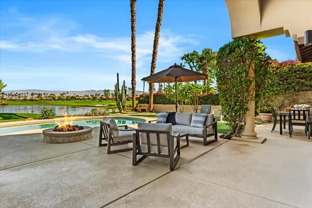 a view of a patio with couches table and chairs under an umbrella with a fire pit