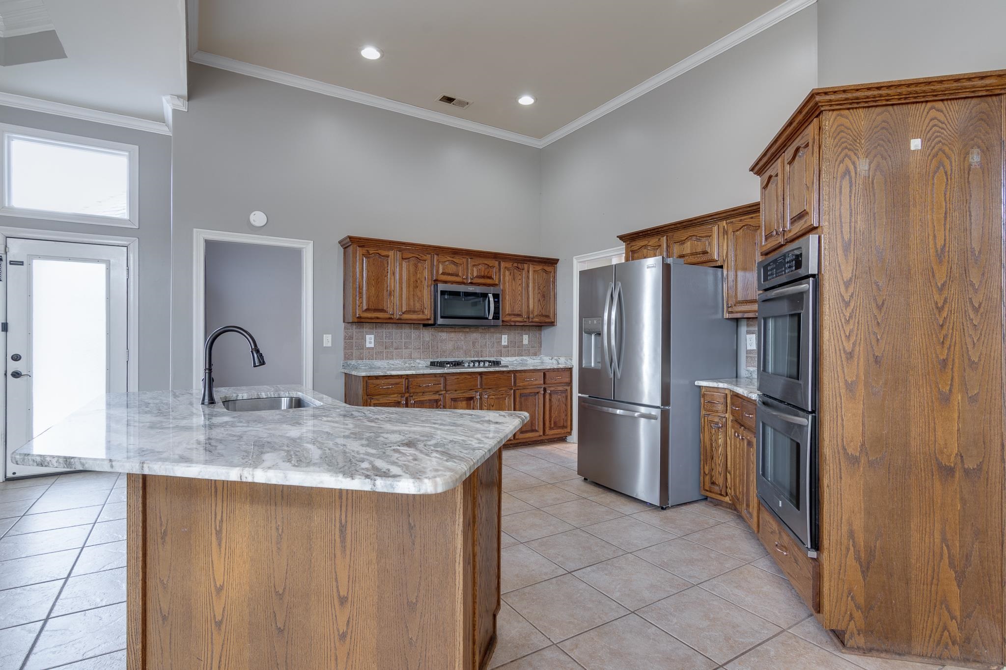 43 Tipton Rdg Cove Munford, TN 38058 - Photo 13 of 30 Kitchen with light tile patterned floors, stainless steel appliances, decorative backsplash, a high ceiling, and wood finish cabinets