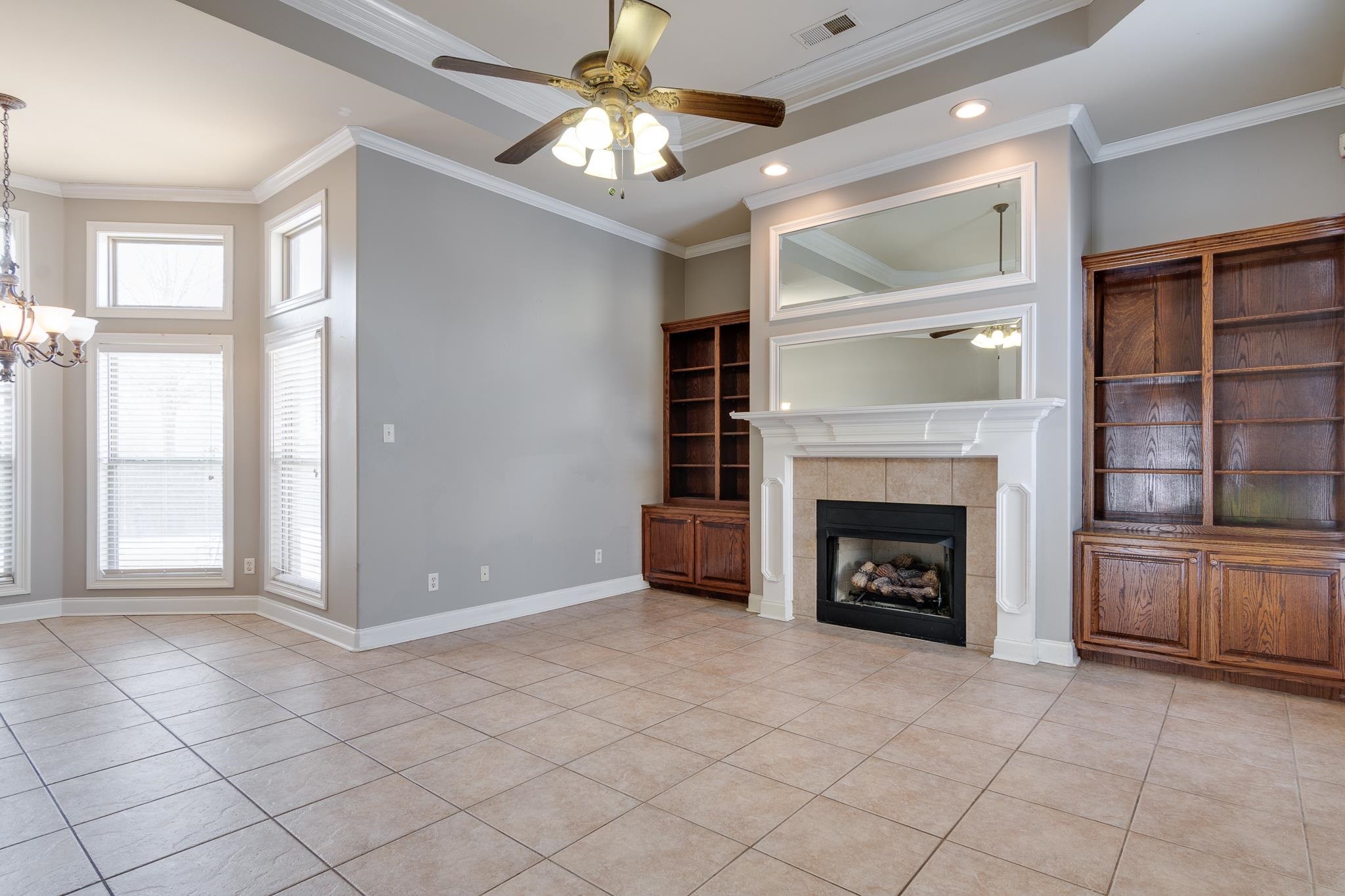 43 Tipton Rdg Cove Munford, TN 38058 - Photo 16 of 30 Unfurnished hearth room featuring ceiling fan, a fireplace, hanging lights, light tile patterned floors, and ornamental molding