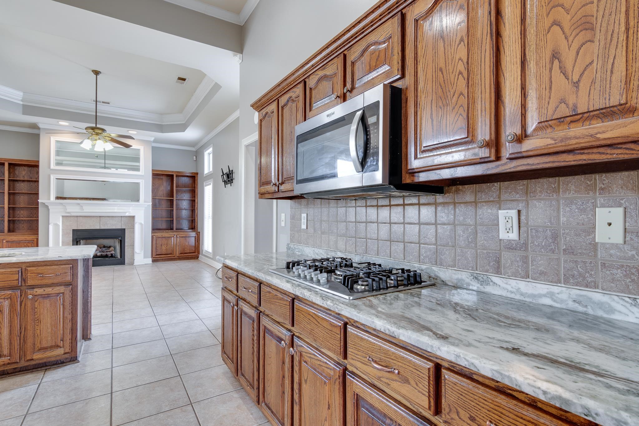 43 Tipton Rdg Cove Munford, TN 38058 - Photo 9 of 30 Kitchen featuring crown molding, backsplash, light tile patterned flooring, wood finish cabinets, and a tray ceiling