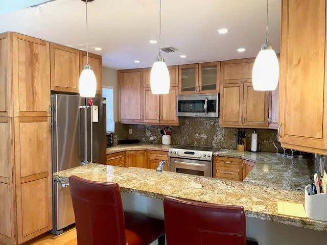 a kitchen with granite countertop a refrigerator a stove a oven a sink with a dining table and chairs