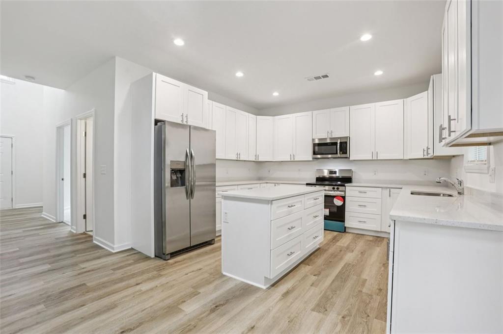 4405 Belcamp Road Fairburn, GA 30213 - Photo 10 of 60 a kitchen with wooden floors white cabinets and stainless steel appliances