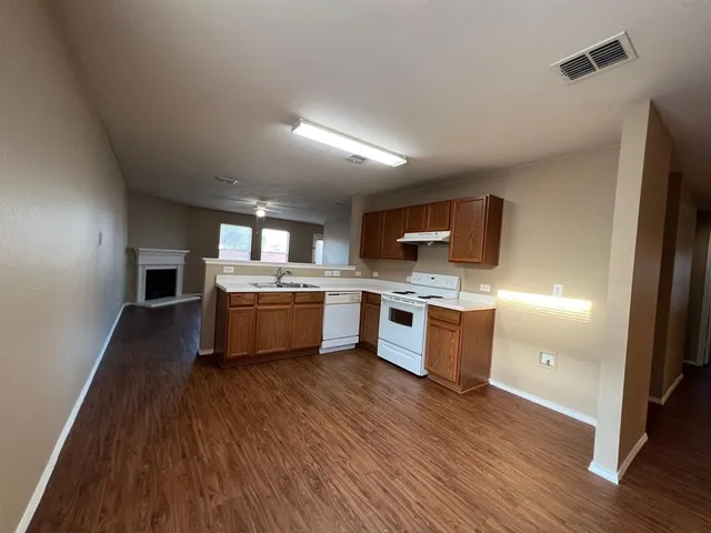 a kitchen with stainless steel appliances a white stove top oven a sink dishwasher and a refrigerator with wooden floor