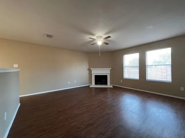 an empty room with wooden floor chandelier fan and windows