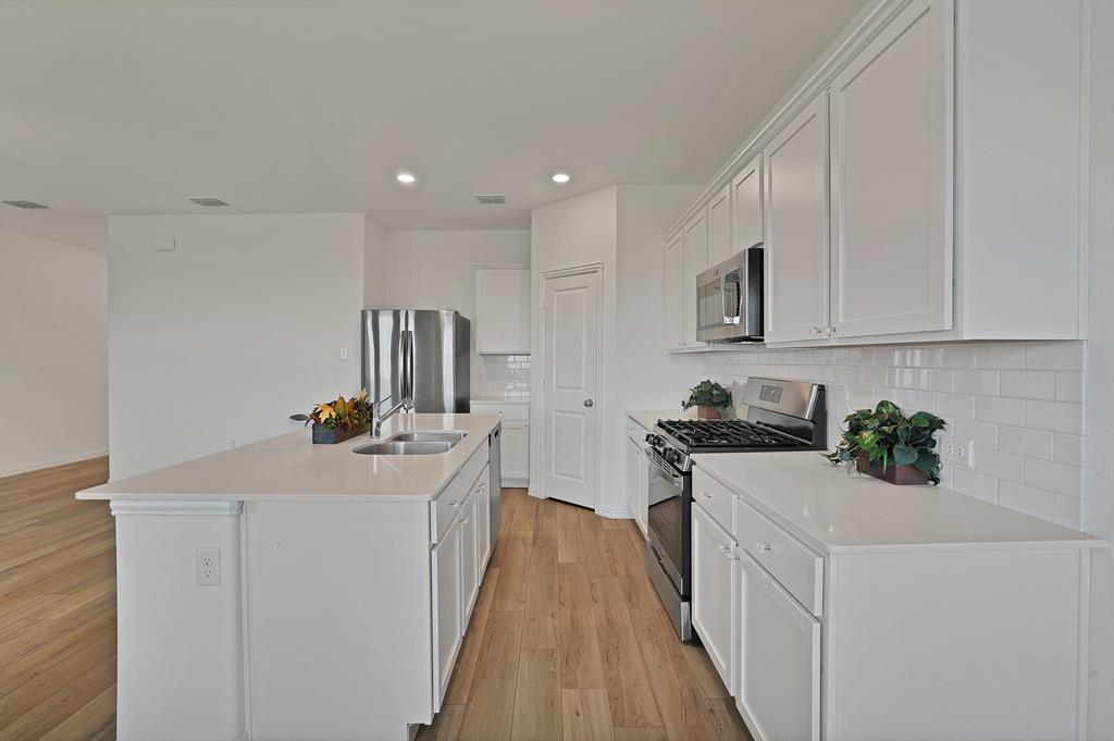 3204 Renaissance Drive Denton, TX 76207 - Photo 8 of 25 Contemporary kitchen with an island featuring a double-basin sink, stainless steel appliances, white cabinetry, and light-toned countertops