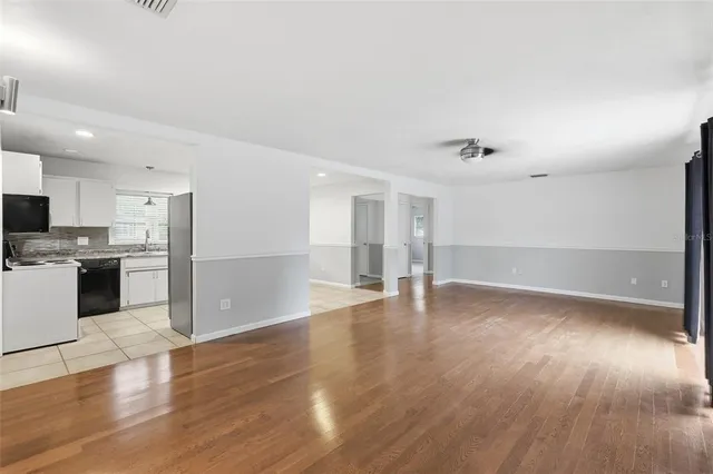 a view of an empty room with wooden floor and a kitchen