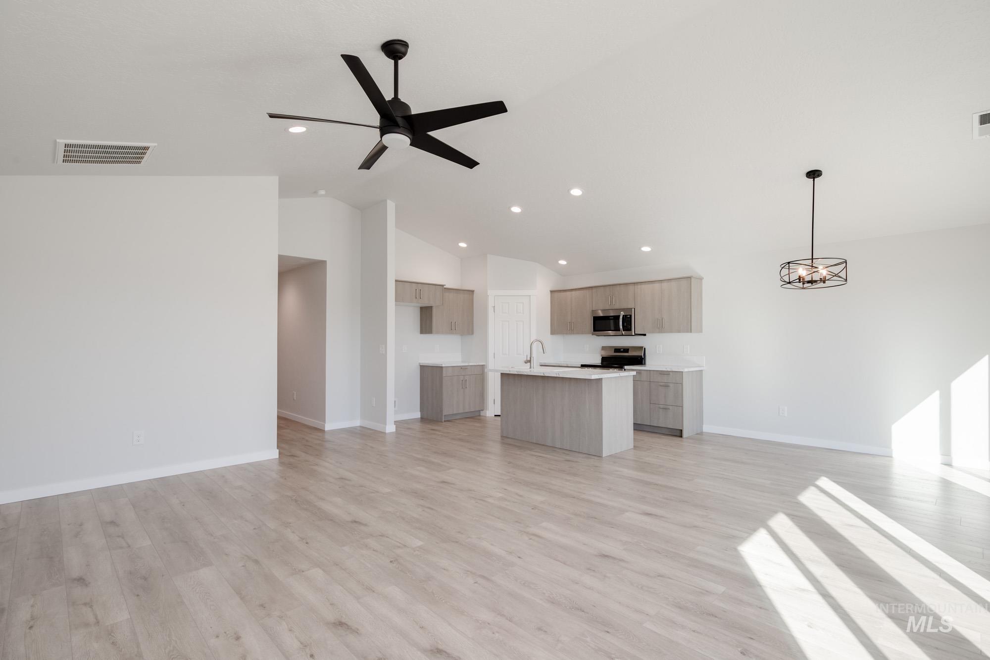 13735 Inman Court Caldwell, ID 83607 - Photo 12 of 22 Unfurnished living room featuring a ceiling fan, light wood-style flooring, hanging lights, and vaulted ceiling