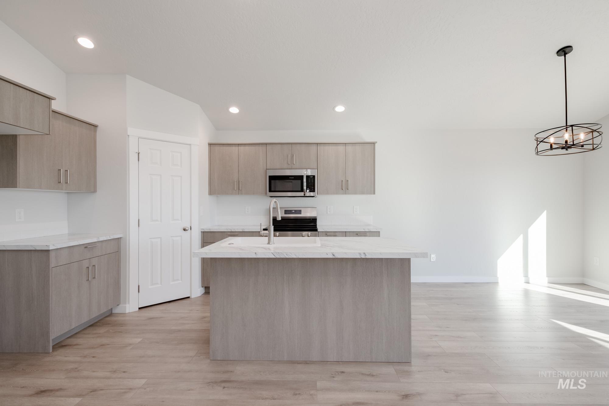 13735 Inman Court Caldwell, ID 83607 - Photo 3 of 22 Kitchen with a kitchen island with sink, light stone counters, light wood-style floors, and pendant lighting