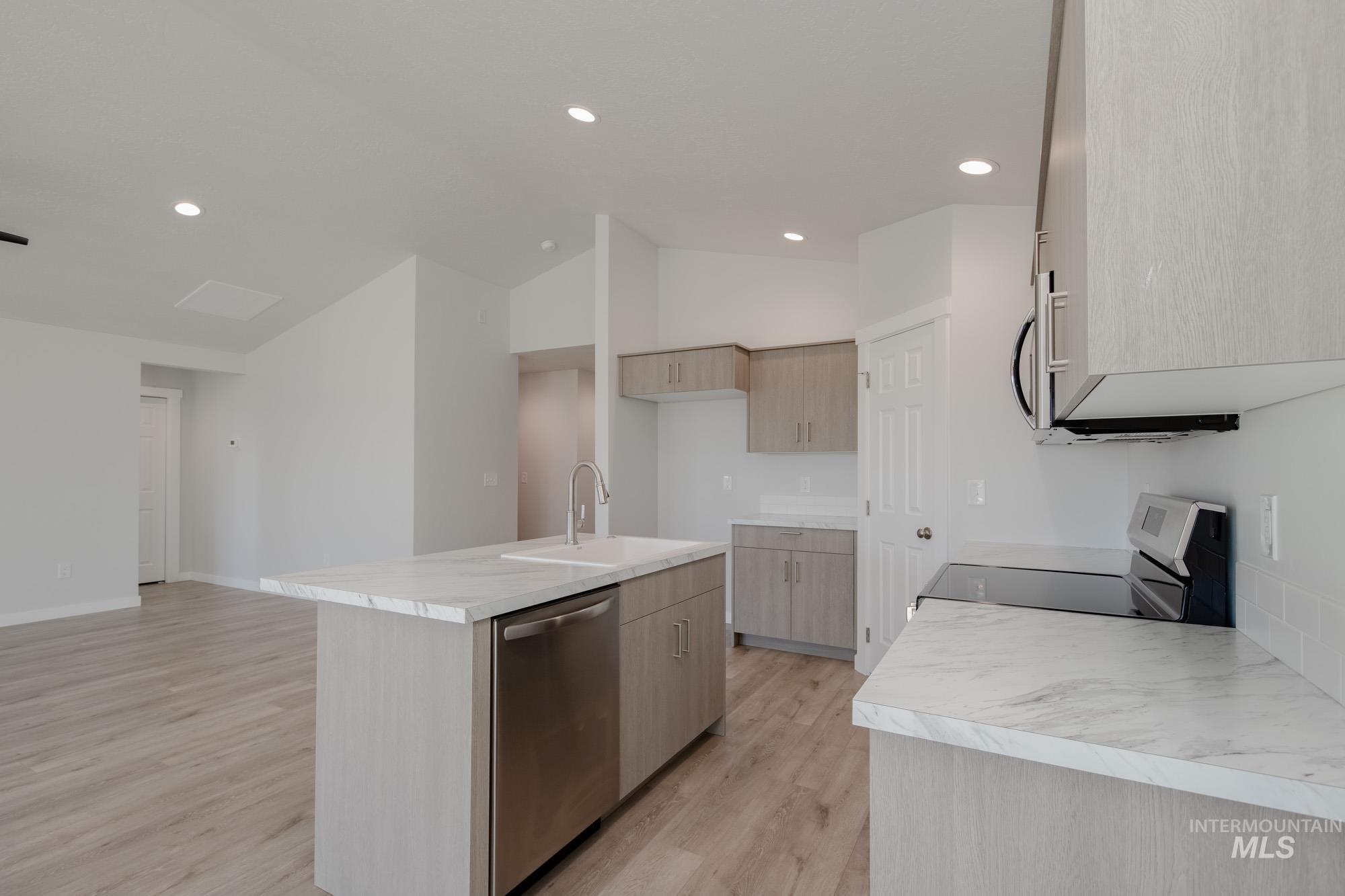 13735 Inman Court Caldwell, ID 83607 - Photo 6 of 22 Kitchen with light countertops, stainless steel appliances, an island with sink, light wood-style floors, and vaulted ceiling