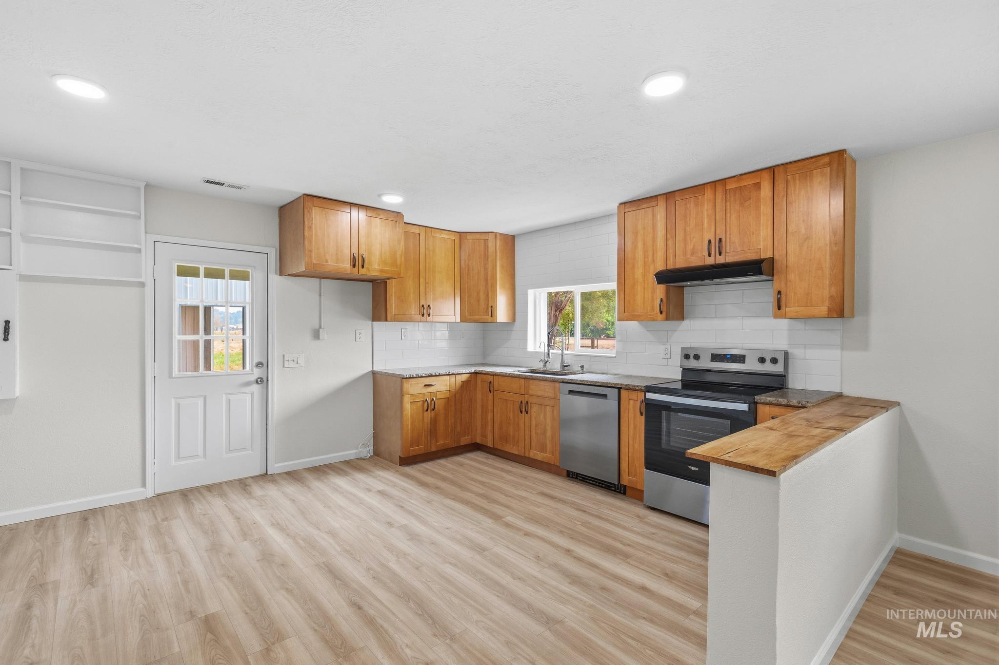 14666 Willis Road Caldwell, ID 83607 - Photo 16 of 50 Open-concept kitchen featuring wood-finish flooring, light wood cabinetry, white subway tile backsplash, stainless steel appliances, and recessed lighting