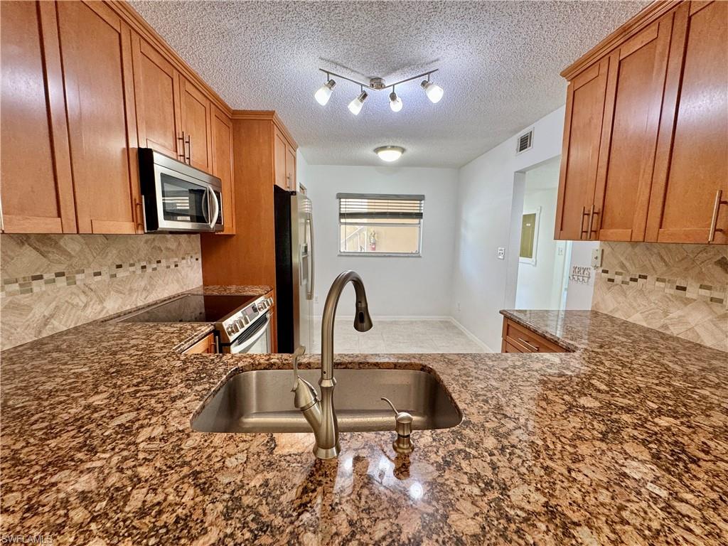 661 Squire Circle, Unit 101 Naples, FL 34104 - Photo 4 of 25 a kitchen with granite countertop a stove a sink and a microwave