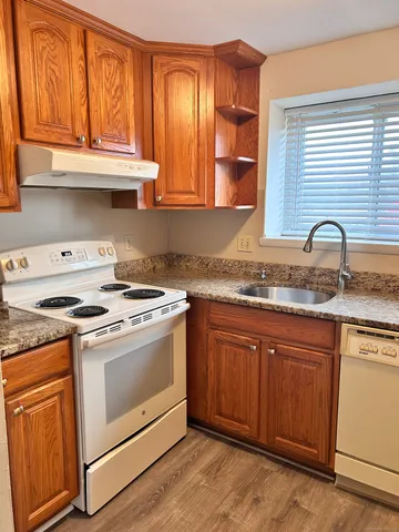 a kitchen with granite countertop a stove a sink and dishwasher wooden cabinets with wooden floor