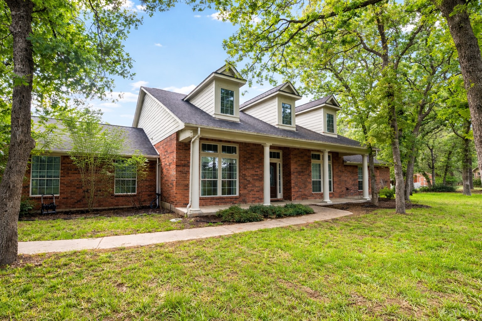The property features a red brick exterior, a covered front porch with white columns, and multiple dormer windows on the roof.