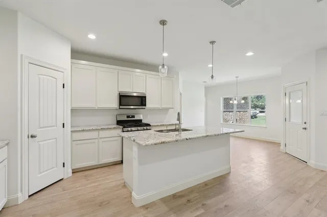 a large kitchen with stainless steel appliances granite countertop a stove a sink and a refrigerator with white cabinets