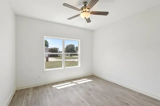 an empty room with wooden floor chandelier fan and windows