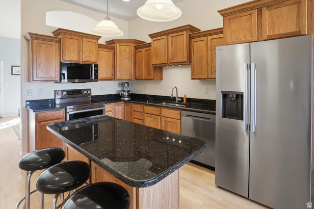 14820 175 East Draper, UT 84020 - Photo 7 of 39 Kitchen featuring stainless steel appliances, brown cabinets, light wood-type flooring, pendant lighting, and dark stone counters