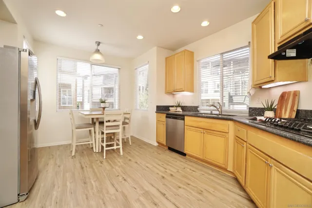 a kitchen with stainless steel appliances granite countertop a refrigerator a sink dishwasher a stove and white cabinets with wooden floor