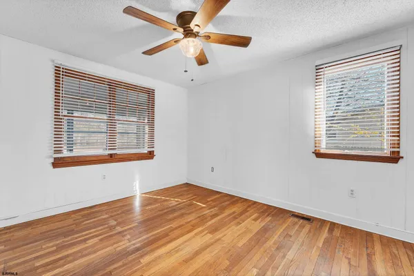 an empty room with wooden floor fan and windows