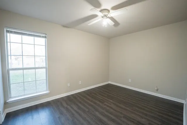 an empty room with wooden floor fan and windows