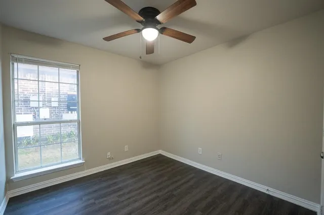 an empty room with wooden floor fan and windows
