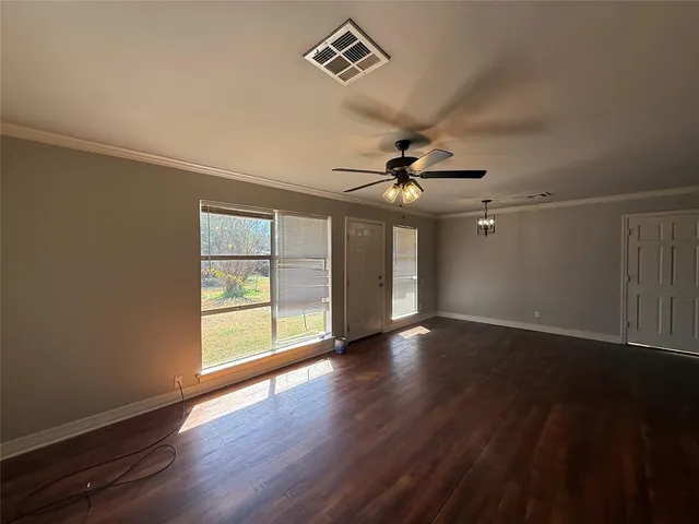 an empty room with wooden floor fan and windows