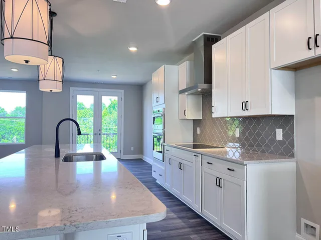 a kitchen with kitchen island granite countertop a stove a sink and white cabinets with wooden floor