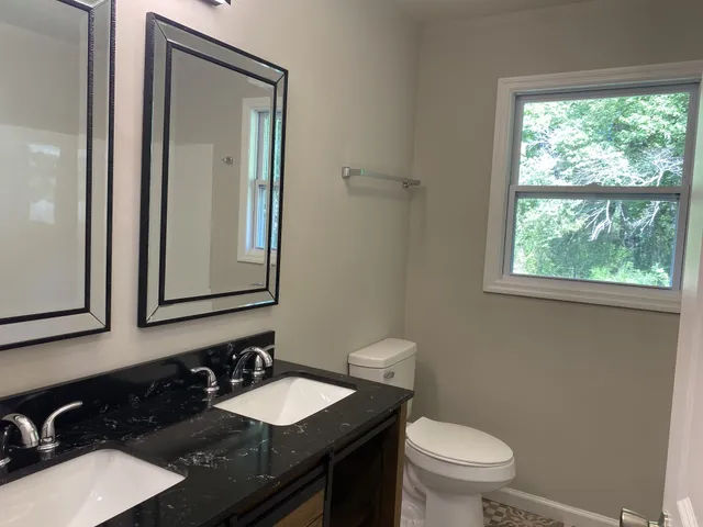 a bathroom with a granite countertop toilet a sink a mirror and a window