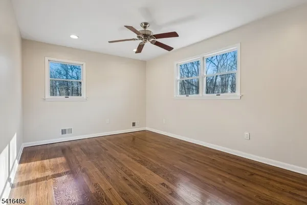 a view of an empty room with wooden floor and a ceiling fan