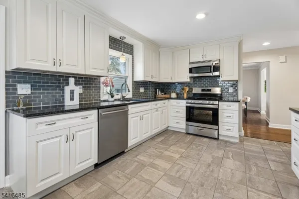 a large white kitchen with stainless steel appliances granite countertop a stove a sink a refrigerator and cabinets