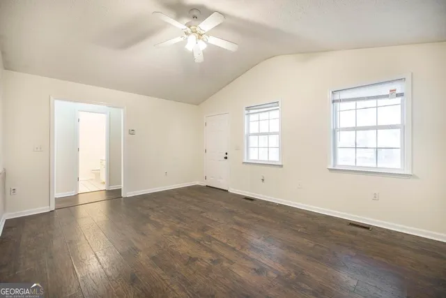 an empty room with wooden floor ceiling fan and windows