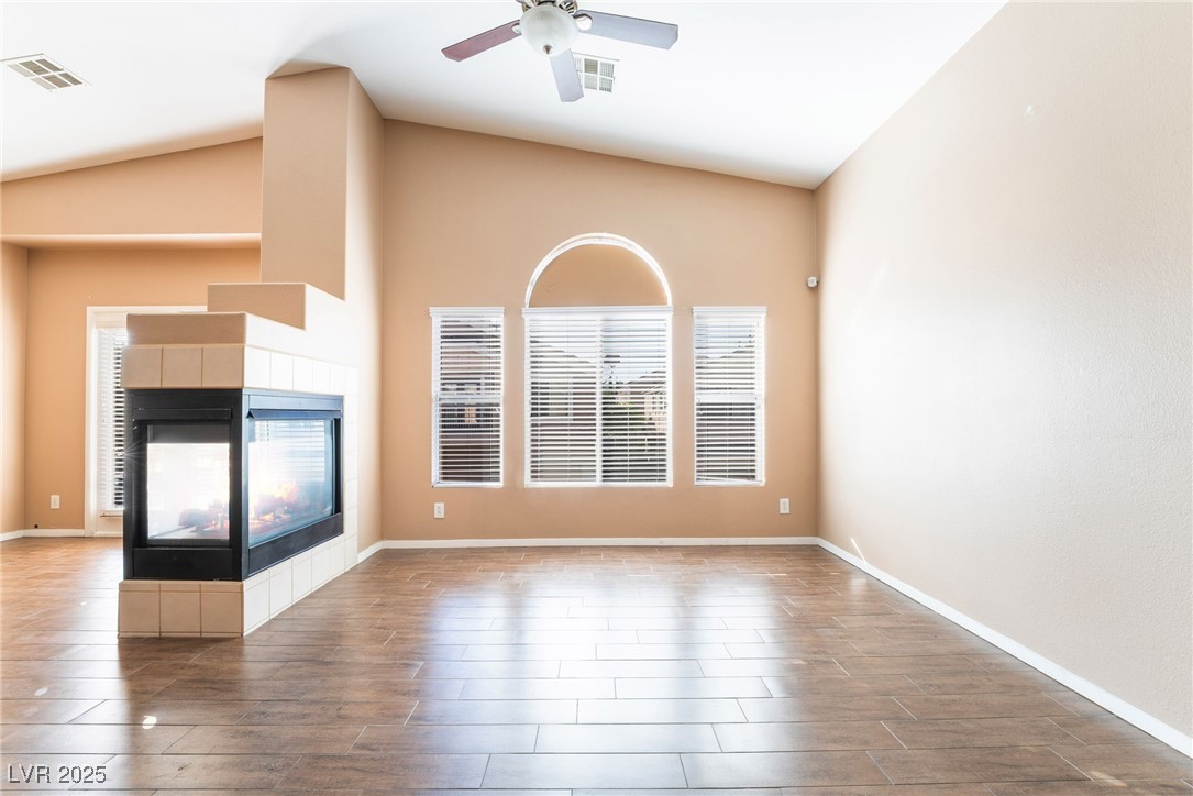 1570 Rusty Ridge Lane Henderson, NV 89002 - Photo 16 of 35 Unfurnished living room with visible vents, a ceiling fan, wood finished floors, a tile fireplace, and lofted ceiling
