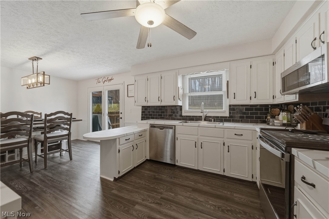 702 Perry Drive Northwest Canton, OH 44708 - Photo 6 of 46 Kitchen featuring stainless steel appliances, a peninsula, a textured ceiling, white cabinetry, and light countertops