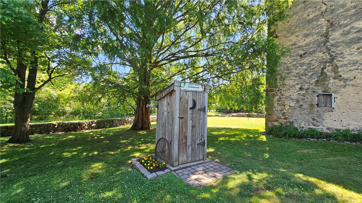585 Buttermilk Road Hellertown, PA 18055 - Photo 61 of 82 A quaint outbuilding nestled within a verdant yard, featuring a rustic stone wall and mature trees.