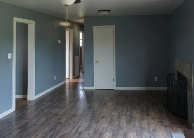 a view of an empty room with wooden floor and a ceiling fan