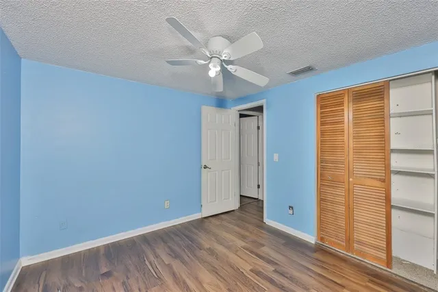 a view of an empty room with wooden floor and a ceiling fan