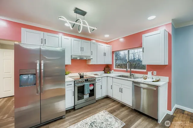 a kitchen with stainless steel appliances granite countertop a refrigerator a sink dishwasher and white cabinets with wooden floor