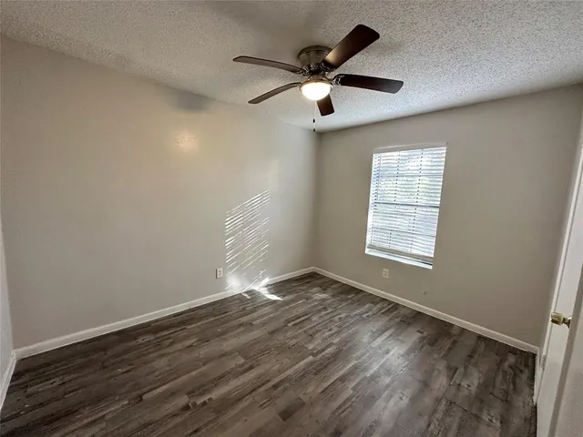 an empty room with wooden floor fan and windows