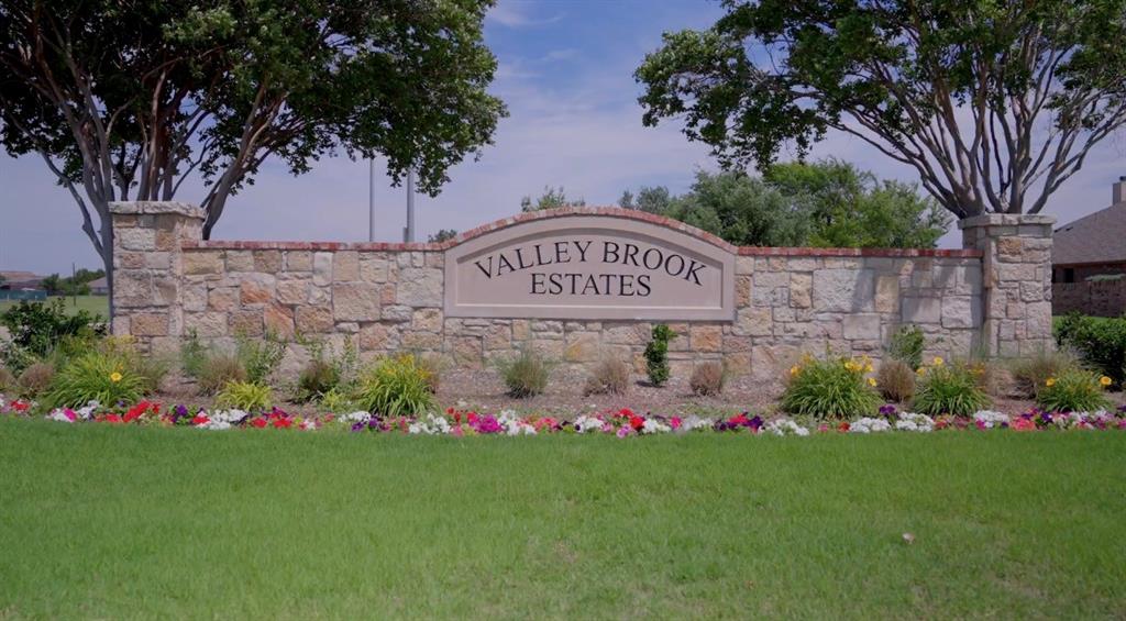Stone entryway sign for Valley Brook Estates, featuring an arched sign panel, stone columns, decorative landscaping, and a manicured lawn