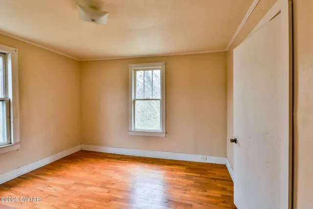 a view of an empty room with wooden floor and a window