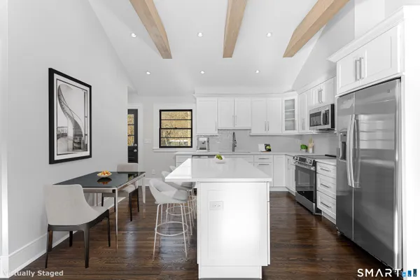a kitchen with stainless steel appliances kitchen island granite countertop a refrigerator a stove a sink a dining table and chairs with wooden floor