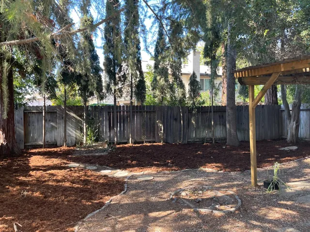 a backyard of a house with large trees and wooden fence