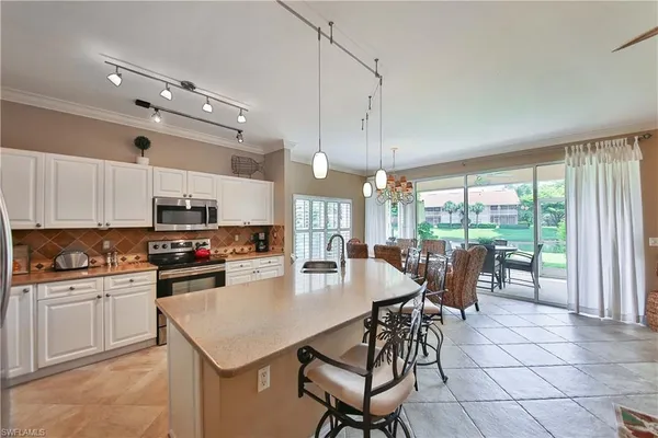 a kitchen with stainless steel appliances granite countertop a stove top oven a sink a dining table and chairs with white cabinets