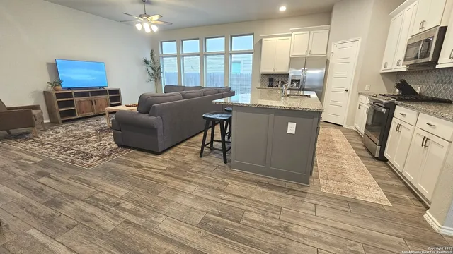 a kitchen with stainless steel appliances granite countertop a stove a sink dishwasher a microwave oven and a dining table with wooden floor